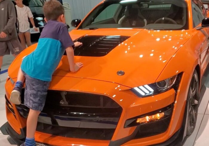 Barn klättrar på huven av en orange sportbil i en bilutställning.