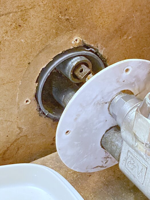 Gammal vattenutkastare med sliten platta och synlig inre mekanism monterad i ett för stort hål i väggen.