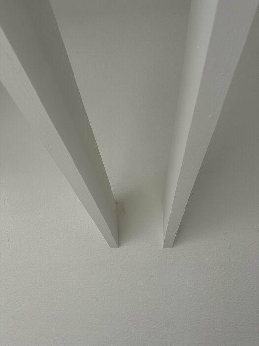 Vit takbjälk som möter ett hörn av ett rum med vitmålade väggar.