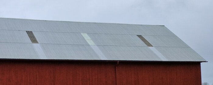 Ett rött ladugårds tak med grön sinus korrugerad aluminiumplåt och skadade glasfiberpartier som släpper in ljus.
