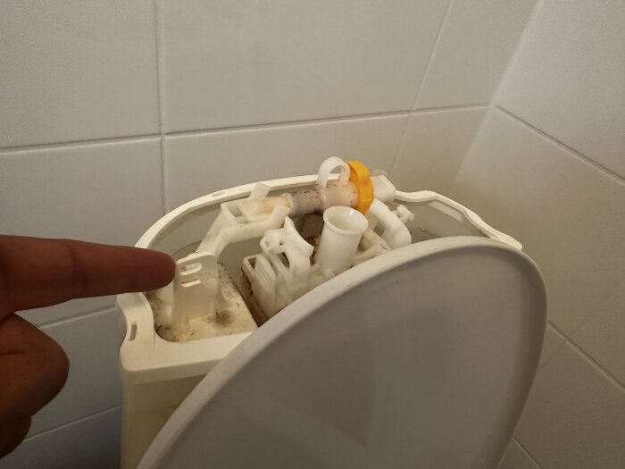 Person som pekar på mekanismen i en toaletts cistern, möjlig fråga om byte av delar.
