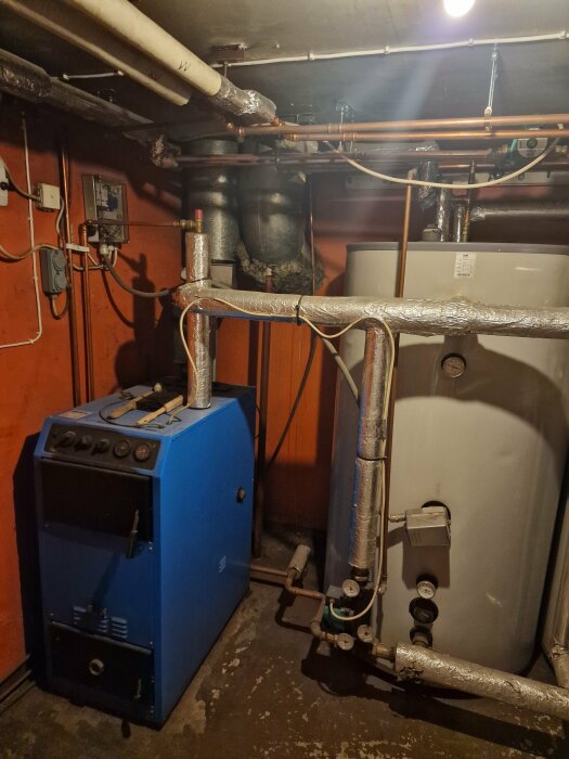 Begagnat vedpannesystem med blå panna och anslutna ackumulatortankar i ett källarutrymme.