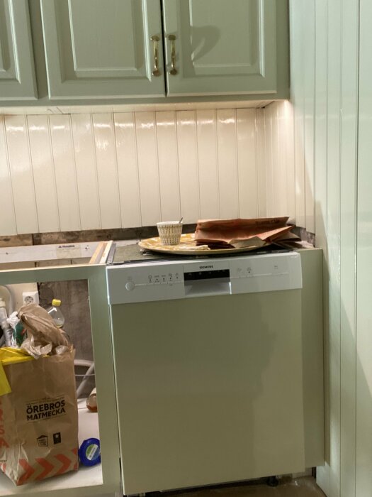 En ny målad diskmaskin i ett kök under renovering med borttagen bänkskiva och pärlspont på väggarna.