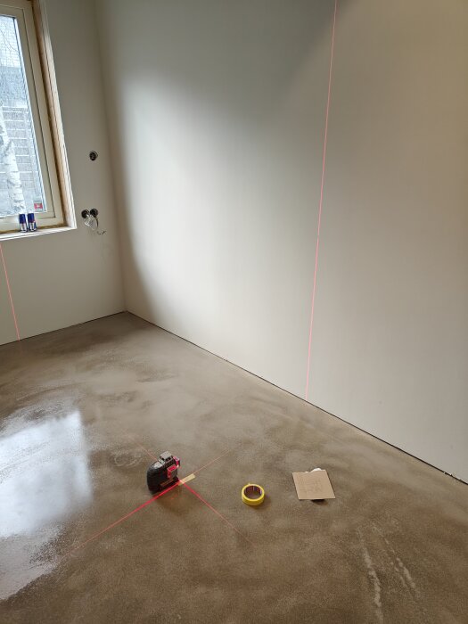 Lasermätverktyg och måttband på betonggolv markerar planering i tomt rum för byggprojekt.