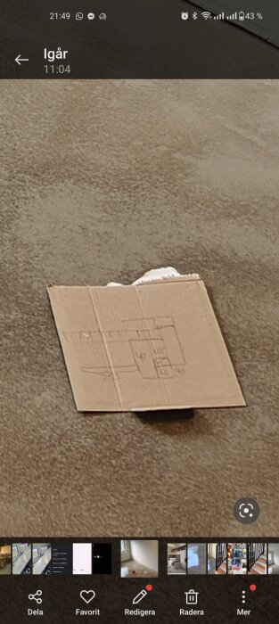 Ritad skiss på en kartongbit som ligger på ett beigefärgat golv, plan för möbelkonstruktion.