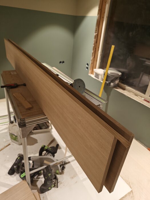 Hyvlat träplank som ska användas som sänggavel, stående på ett arbetsbord i ett rum under renovering.