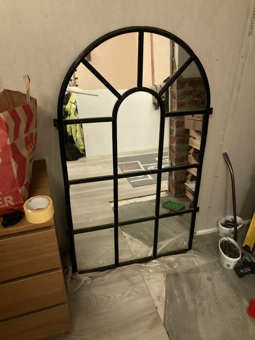 Spegel designad som ett gammalt stallfönster mot tegelvägg, omgiven av renoveringsmaterial.