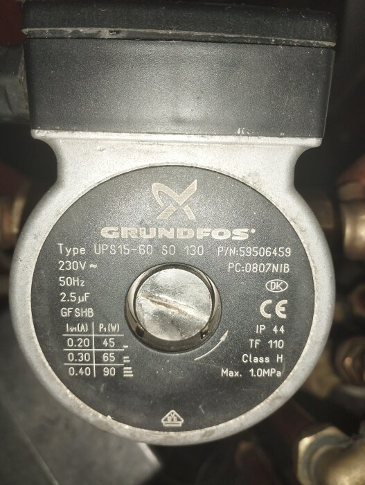 Grundfos cirkulationspump med tekniska specifikationer synliga på etiketten, som omges av VVS-komponenter.