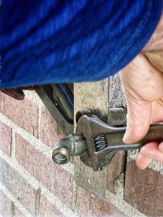 Person demonterar en mutter med en justerbar skiftnyckel från en rördel vid en tegelvägg.