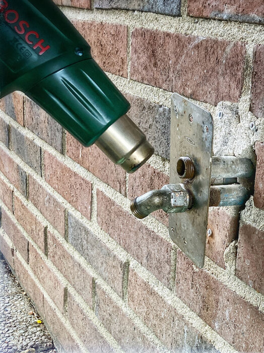 Värmepistol appliceras på metallfästanordning på tegelvägg under renoveringsarbete.