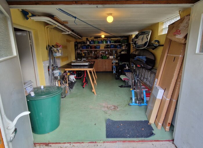 Interiör av ett garage använt som verkstad med arbetsbänk, verktyg och förvaringshyllor.