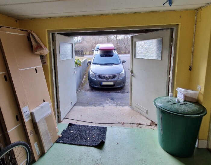 Garage med öppen dörr som visar bil utanför, ventil högt på vägg och potentiella platser för luftintag.