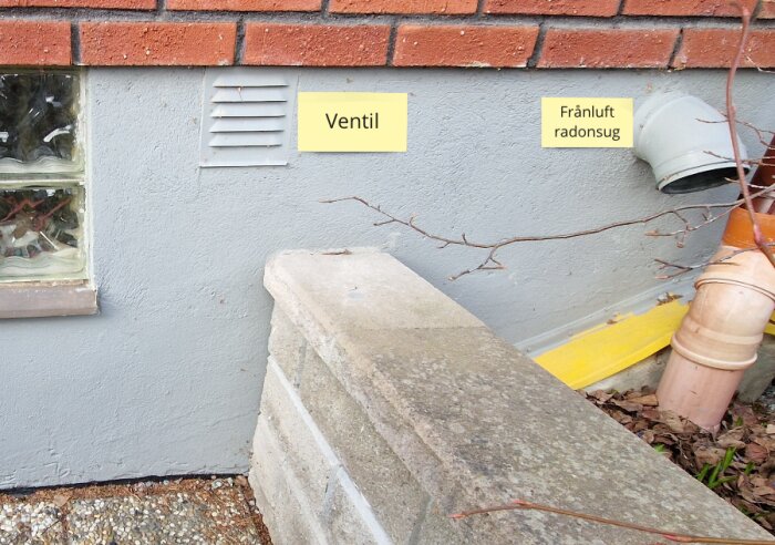 Vägg med ventil bredvid fönster och frånluftsrör för radonsug på husfasad.