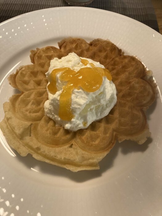 Nygräddad våffla med grädde och sylt på en vit tallrik.