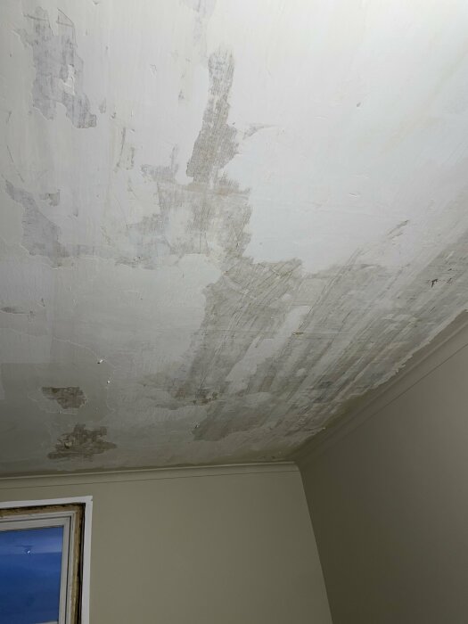Innertak med skadat pappspänt tak som har flagnande målarbeten och synliga reparationer.