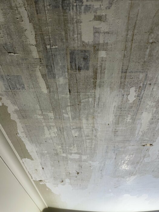 Delvis renoverat innertak med skadat och krackelerat lager av färg, synliga reparationer och papperslappar, indikerar renoveringsproblem.