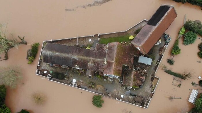 Flygbild på ett hus omgivet av en skyddsmur under en översvämning.
