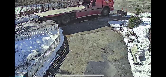 Röd bärgningsbil på en gårdsplan omgiven av snö och staket, märkningen på bilen är otydlig.