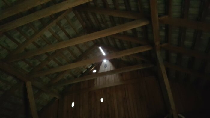 Utsikt inifrån en lada med synliga träbjälkar och ljus som silas in genom sprickor i taket.