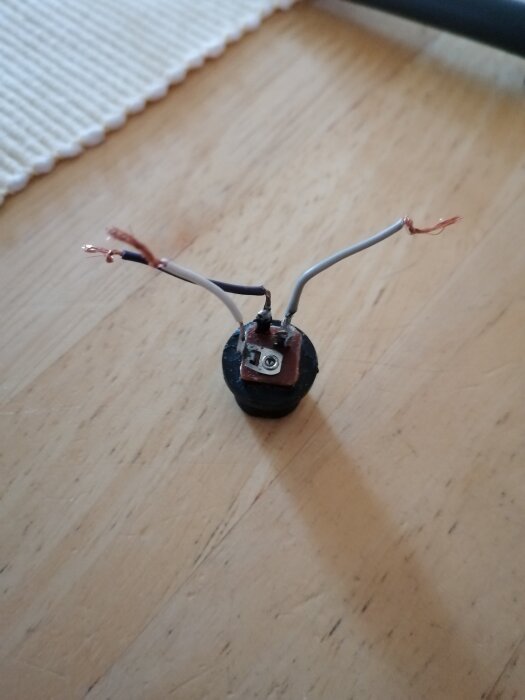 Transformator till motionscykel med avskalade trådar och synlig terminal på trägolv.