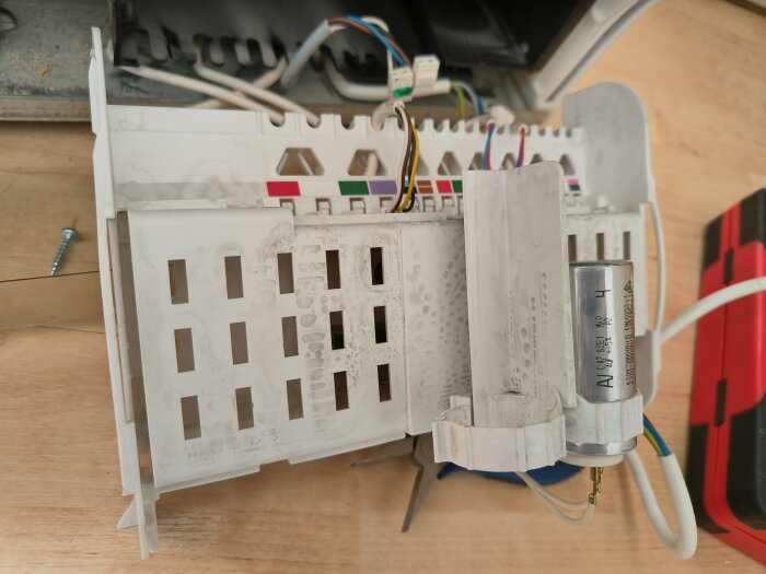 Öppet vitt plasthölje med kablar och en cylindrisk komponent, troligen en kondensator, nära en kompressor.