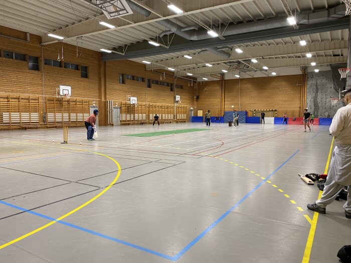 Barn och vuxna spelar innebandy i en idrottshall med träväggar och basketkorgar.