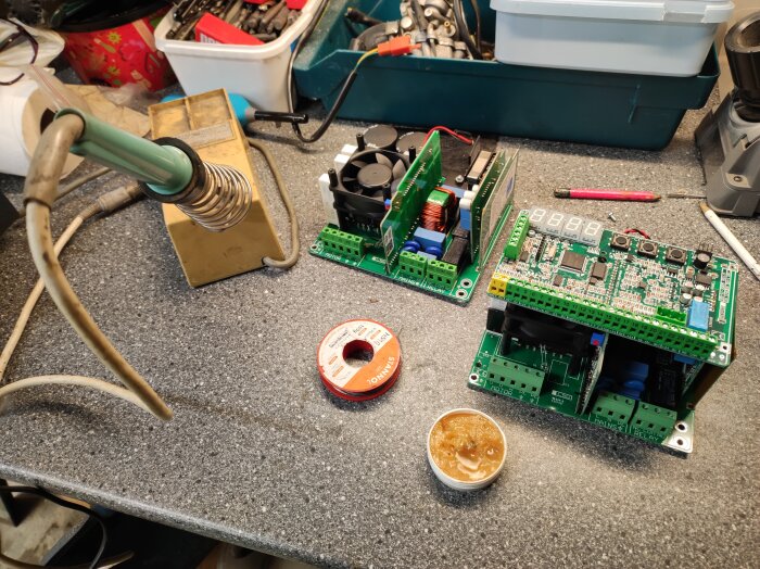 Antik lödstation bredvid öppna elektroniska enheter och lödtenn på ett arbetsbord vid reparation.