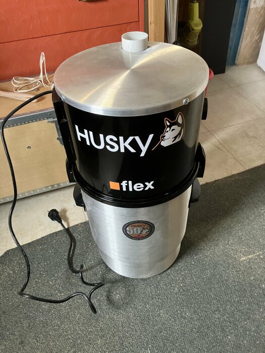 Centraldammsugarenhet Husky Flex står på golvet med logotyp och anslutningskoppling.