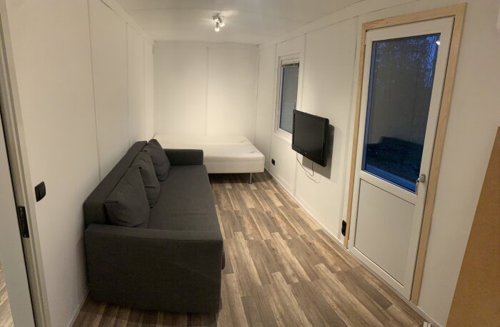 Nyrenoverat rum redo för uthyrning med en soffa, säng och TV på väggen.