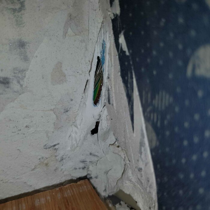 Skadad vägg med en synlig öppning där ledningar och isolering är delvis exponerade.