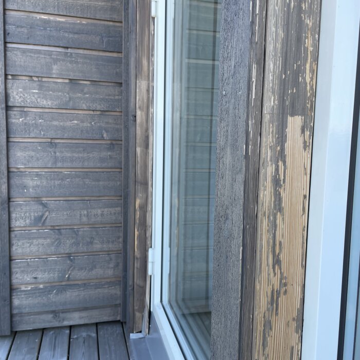 Träpanel med flagnande grå lasyr, synlig trägrund och vit fönsterram, illustrerar problem med lasyrkvalitet efter två år.