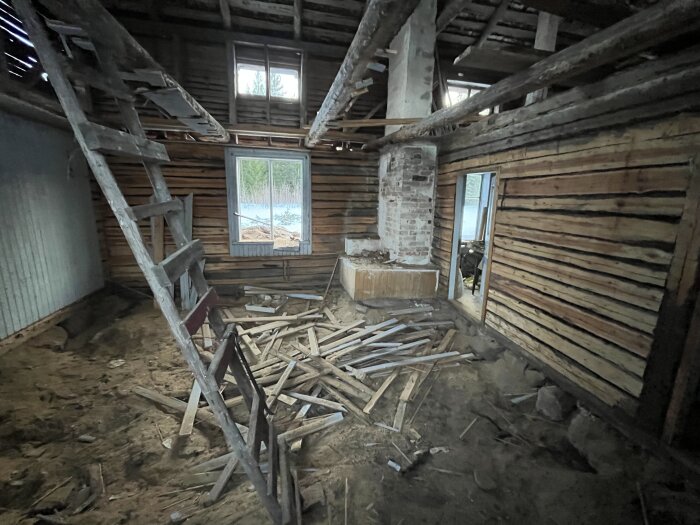 Förfallen interiör av ett gammalt hus med rutten bjälke nära väggen, bråte på golvet och en stege.