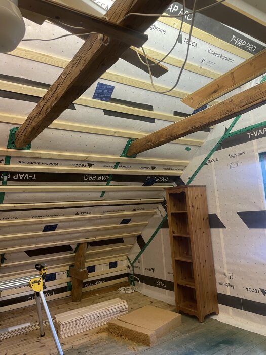 Tak med träbjälkar och stödben där gipsskivor ska monteras, tomma väggsektioner och isoleringsmaterial.