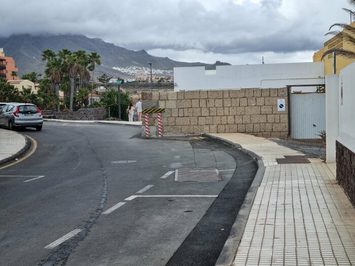 Mur längs trottoaren i ett urbant landskap med berg i bakgrunden.