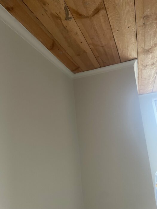 Renoverat rumshörn med nytt träbjälklag i taket och nymålade vita väggar.