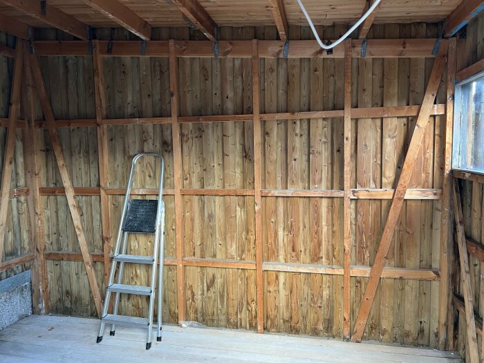 Tomt förråd med synliga träreglar, isoleringsluckor i tak, trappa och fönster.