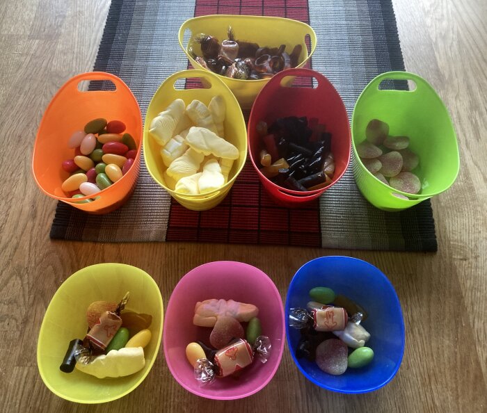 Olika sorters godis sorterade efter färg i sex färgglada skålar på ett bord med löpare.