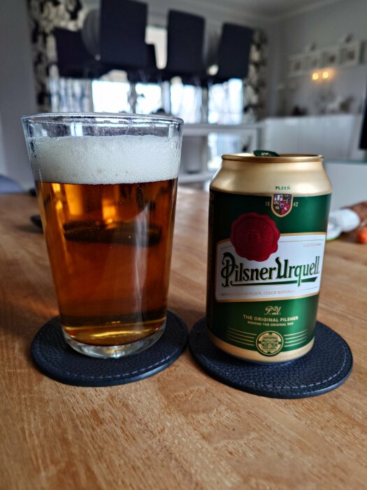 Ett glas med öl bredvid en Pilsner Urquell burk på ett bord.