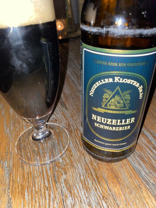 Ett glas mörkt öl och en flaska Neuzeller Schwarzbier på ett träbord.