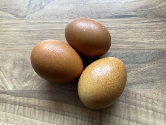 Tre bruna ägg på ett träbord med synliga ådror.