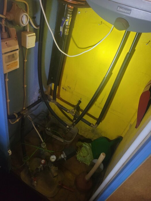 Vattenpump och rörledningar i ett pumprum med gula väggar, synlig mätare och elektriska dosor.