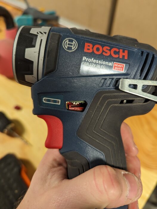 Hand håller en Bosch skruvdragare med en trasig knapp för ändring av rotationsriktning.