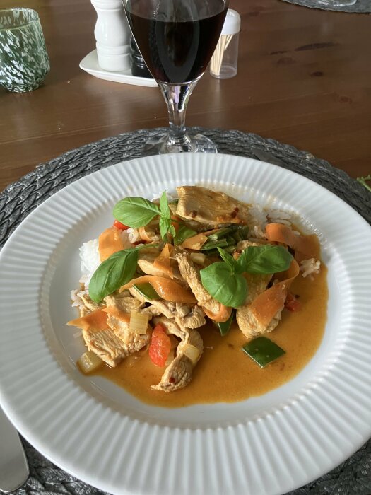Paneng Red Curry med kyckling, lök och selleri serveras på vit tallrik med ris och basilikablad.