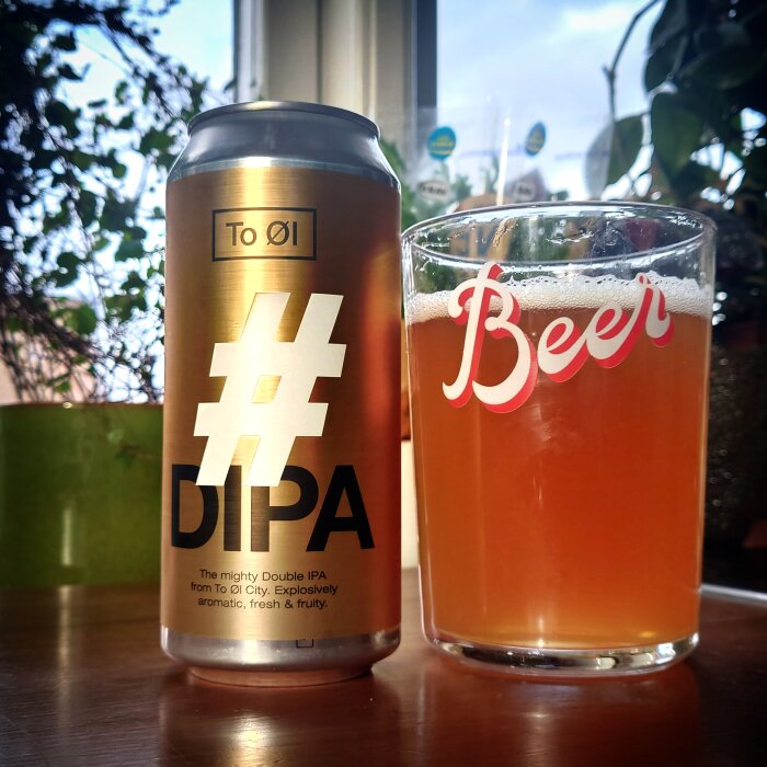 En burk Double IPA öl bredvid ett glas med öl framför ett fönster, med texten "#DIPA" på burken.
