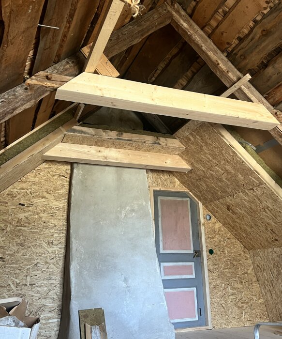Oisolerat tak med träbjälkar och en skorsten, nybyggda stöd nära en dörr, indikation på ombyggnation för ventilation.