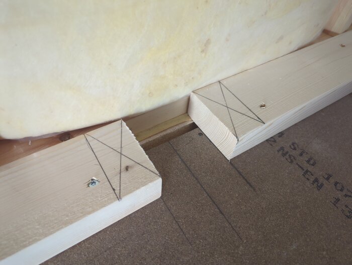 Ny regling framför befintlig glasullsisolering med markerade linjer på undergolv för bygge av akustikvägg.