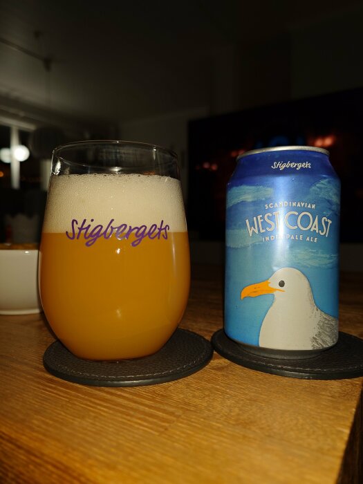 Ett glas med öl och en ölburk från Stigbergets med texten 'West Coast' och en bild av en mås.