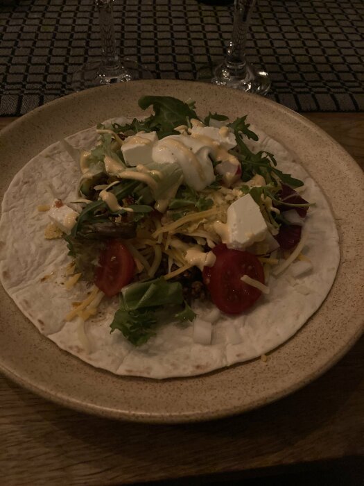 En öppen taco med sallad, köttfärs, ost, gräddfil och tomat på en tallrik.