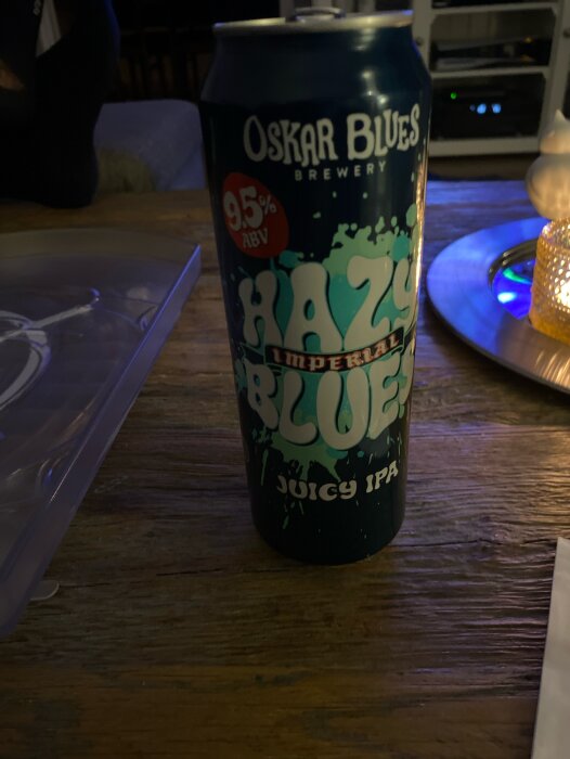 En ölburk från Oskar Blues Brewery med texten 'HAZY' och '9.5% ABV' på ett bord i ett dunkelt rum.