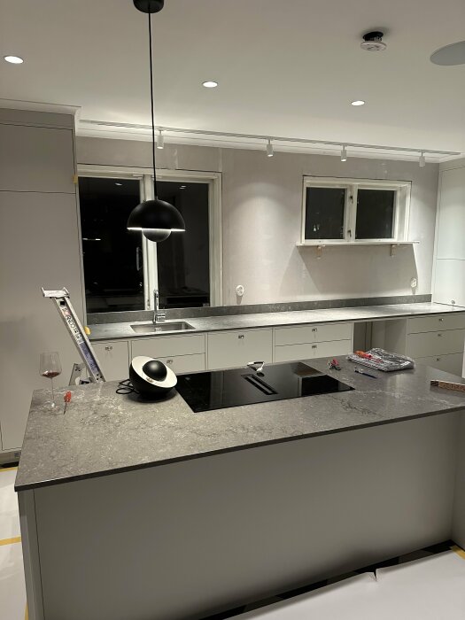Nyligen renoverat kök med grå skåp, stenbänkskiva och inbyggda vitvaror; taklampor delvis installerade.